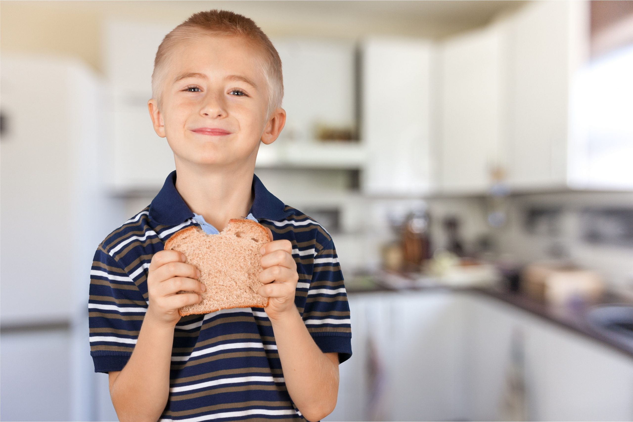 Little boy eating peanut butter sandwich in the kitchen