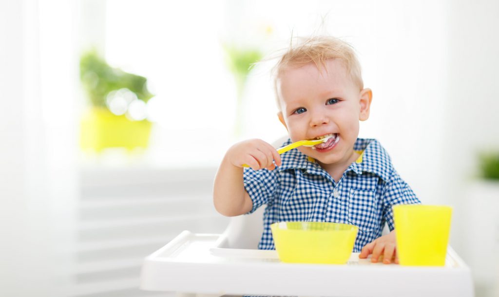 Happy baby eating himself with a spoon
