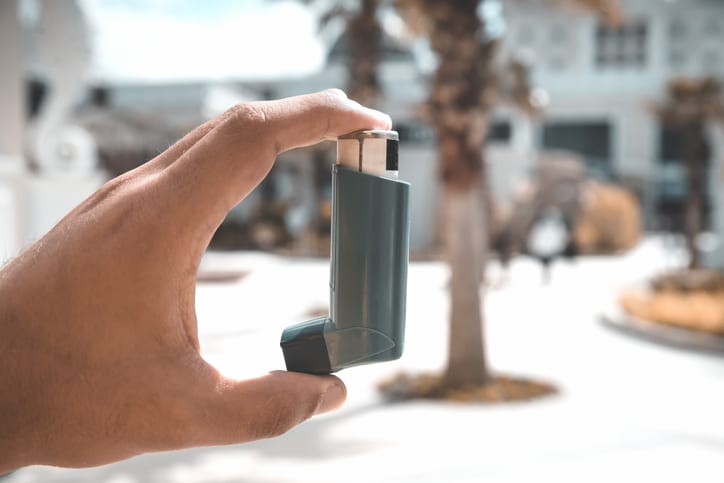 Young man using an asthma inhaler outdoors.