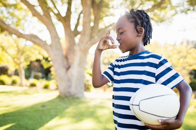 Child outside with football using inhaler
