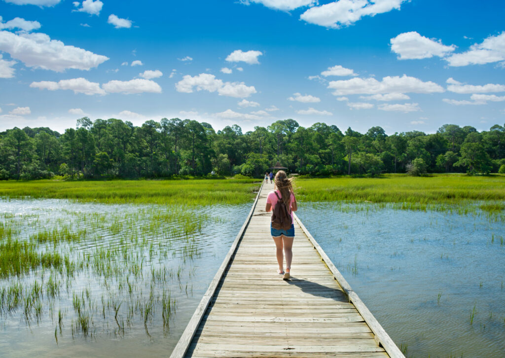 Girl with backpack walking on boardwalk in the marsh