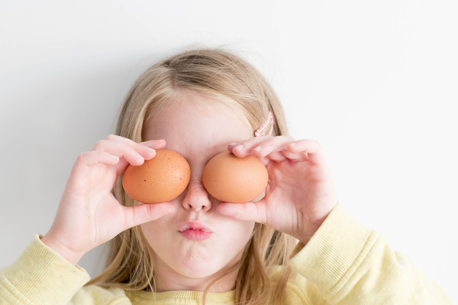 child holding brown eggs in front of her eyes