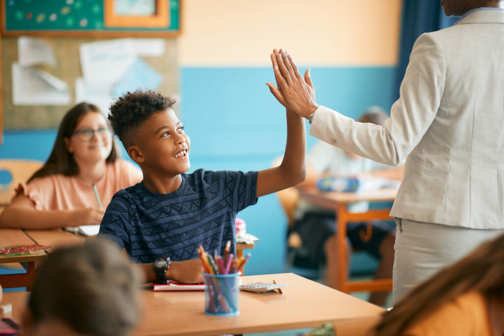 Happy African American schoolboy giving high-five to his teacher during class in the classroom